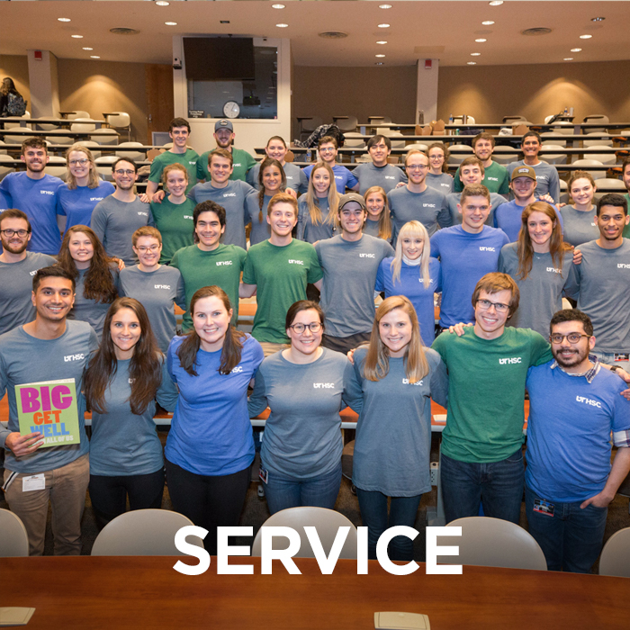 Large group of students pose for photo while wearing shirts from a service project. The word "service" is imposed on the lower part of the photo.