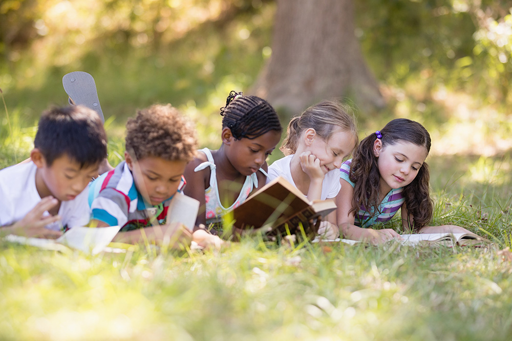 Children laying in the grass outside reading.