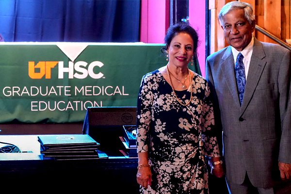 Male and female faculty member stading  before a GME banner and table