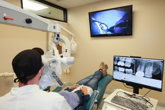 Endodontist working on patient's teeth as they watch on a screen.