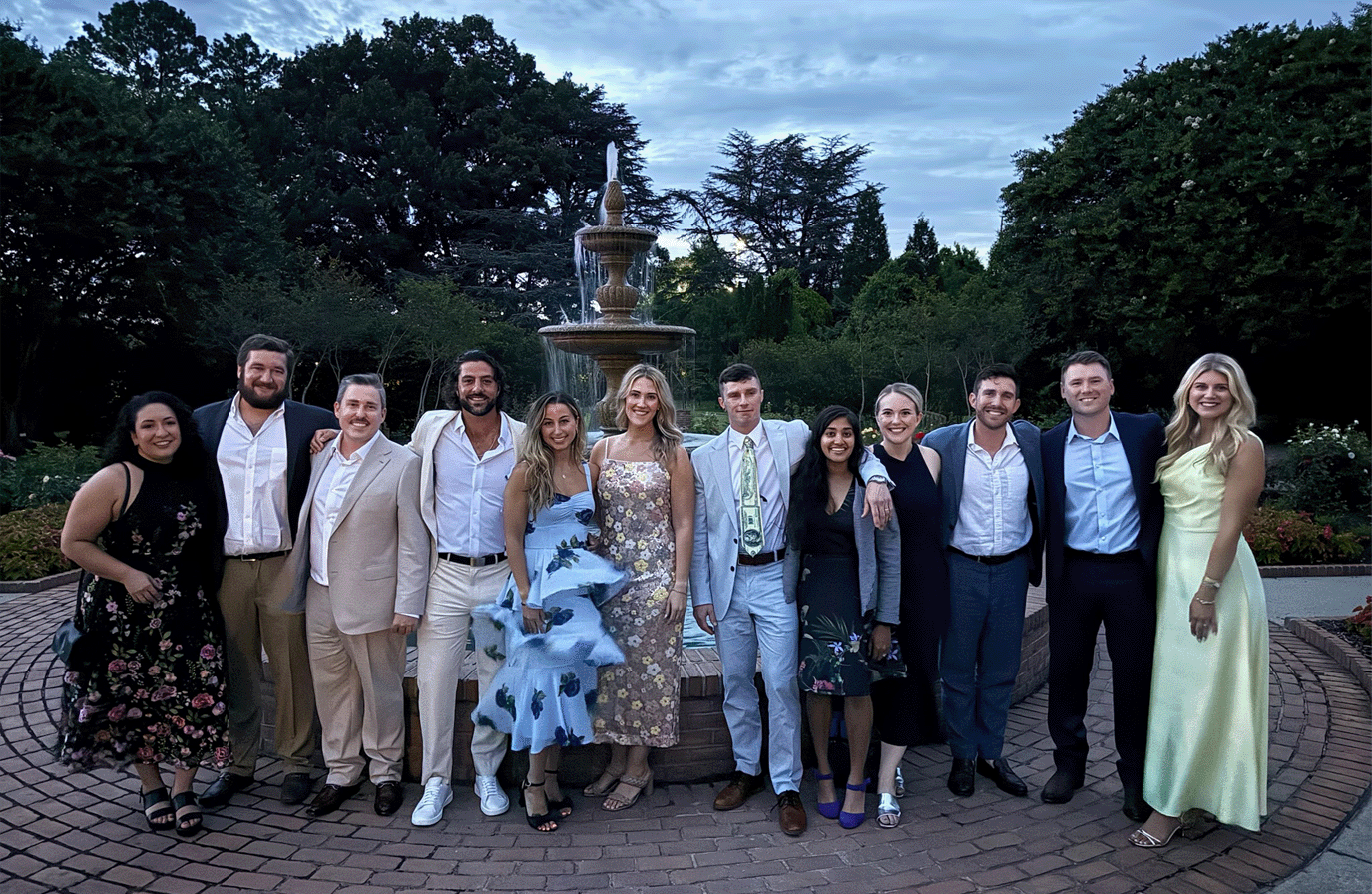 Emergency medicine graduates posing together outdoors in front of a tiered fountain