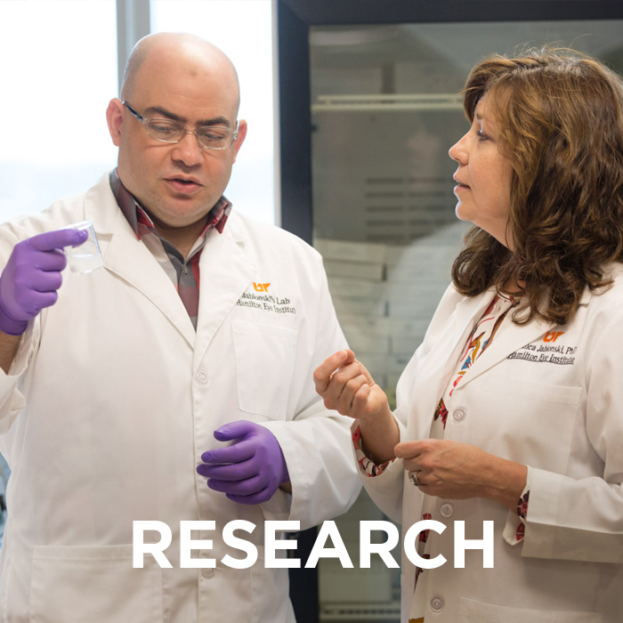 Researchers discussing in a lab. The word "research" appears over the image. Click this image to view pages on research at Hamilton Eye.