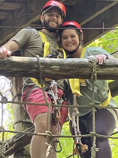 Male and female resident on a platform before ziplining from a tree outdoors