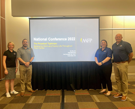 Faculty in front of a display at national conference