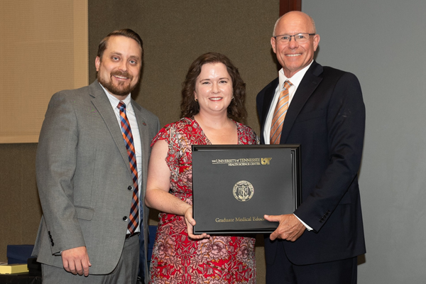 Resident holding a certificate with faculty at graduation