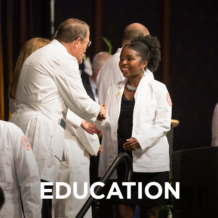 Male student shaking the dean's hand at white coat ceremony. The word "education" is imposed on the lower part of the image.