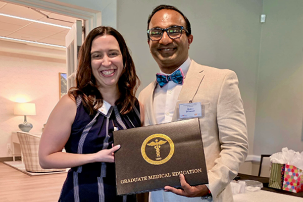 Female graduate holding her certificate while standing with program director