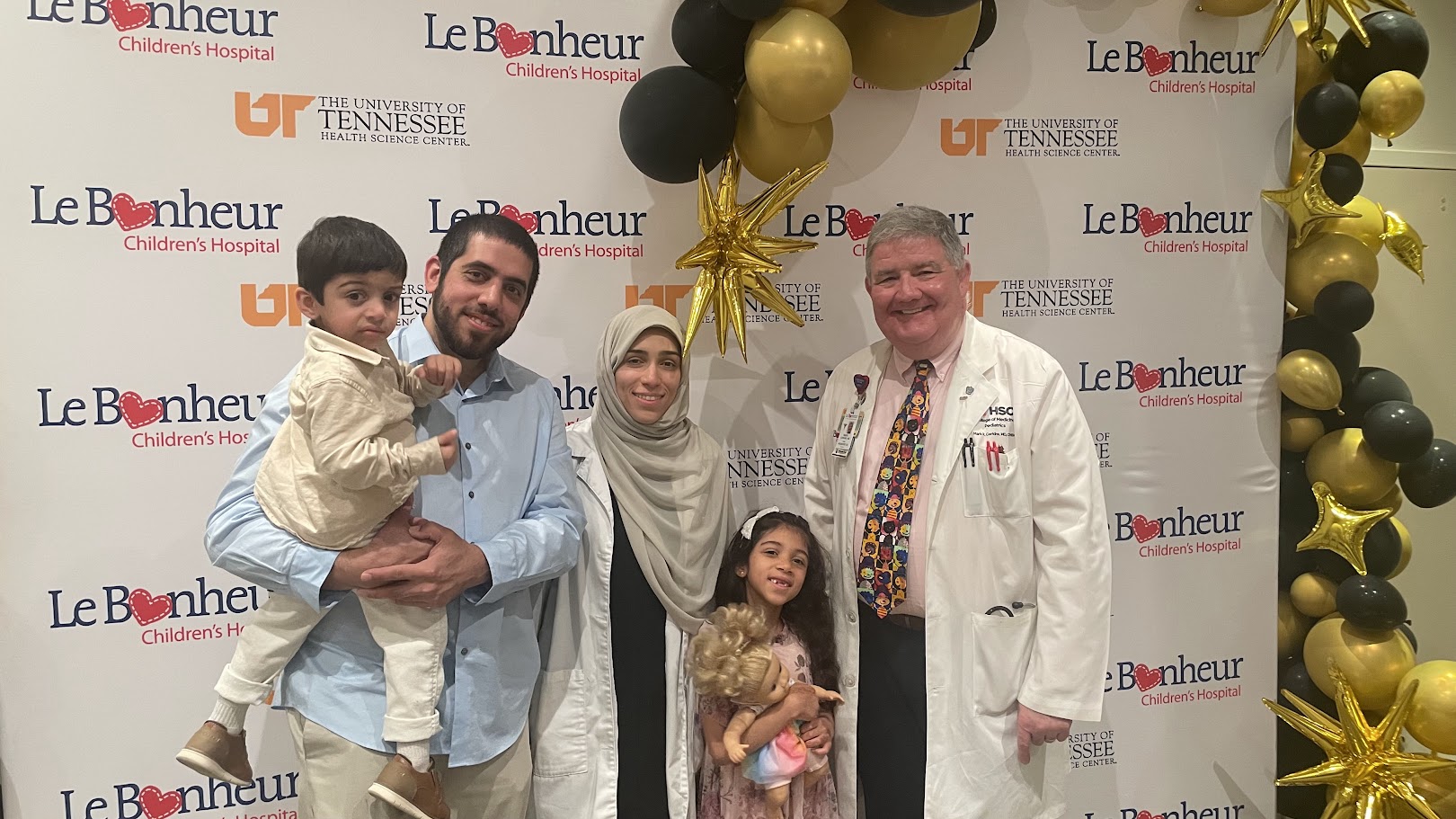 Fellow, their family, and a faculty member in front of a Le Bonheur background