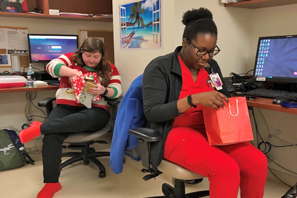 Two female residents sitting in an office opening gifts