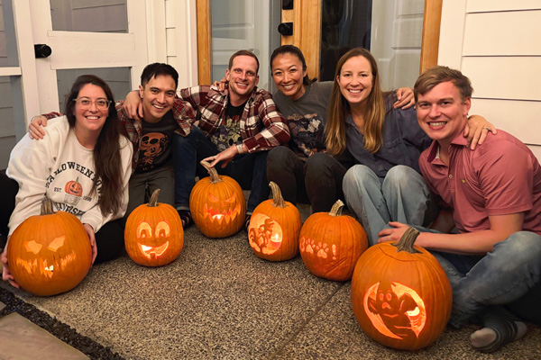 Group of fellows posing with carved pumpkins on a porch during a fall gathering