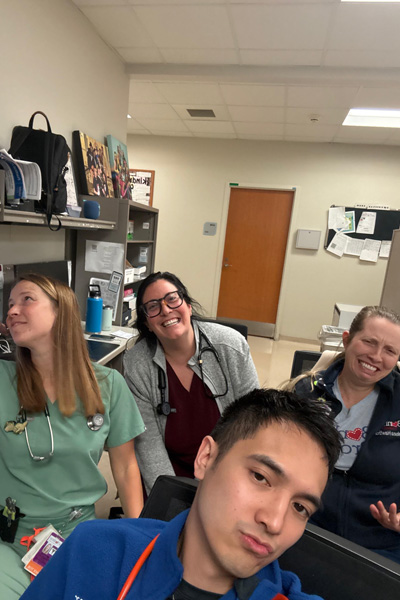 Four fellows pose playfully for a selfie in a clinical workroom with desks and computer workstations