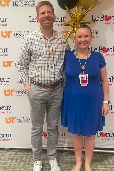 Faculty posing with recent graduate in front of a Le Bonheur background
