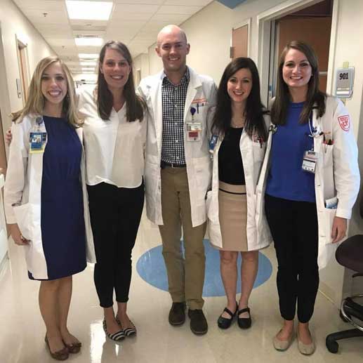 Five smiling residents in the hospital hallway