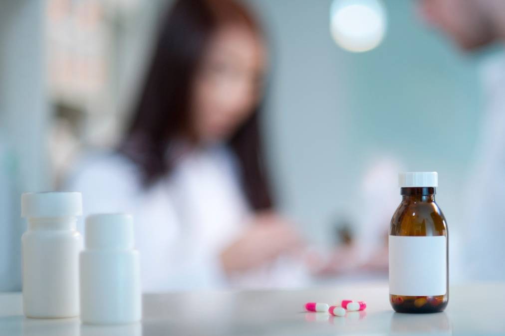 Medicine in foreground, blurry pharmacist in background.