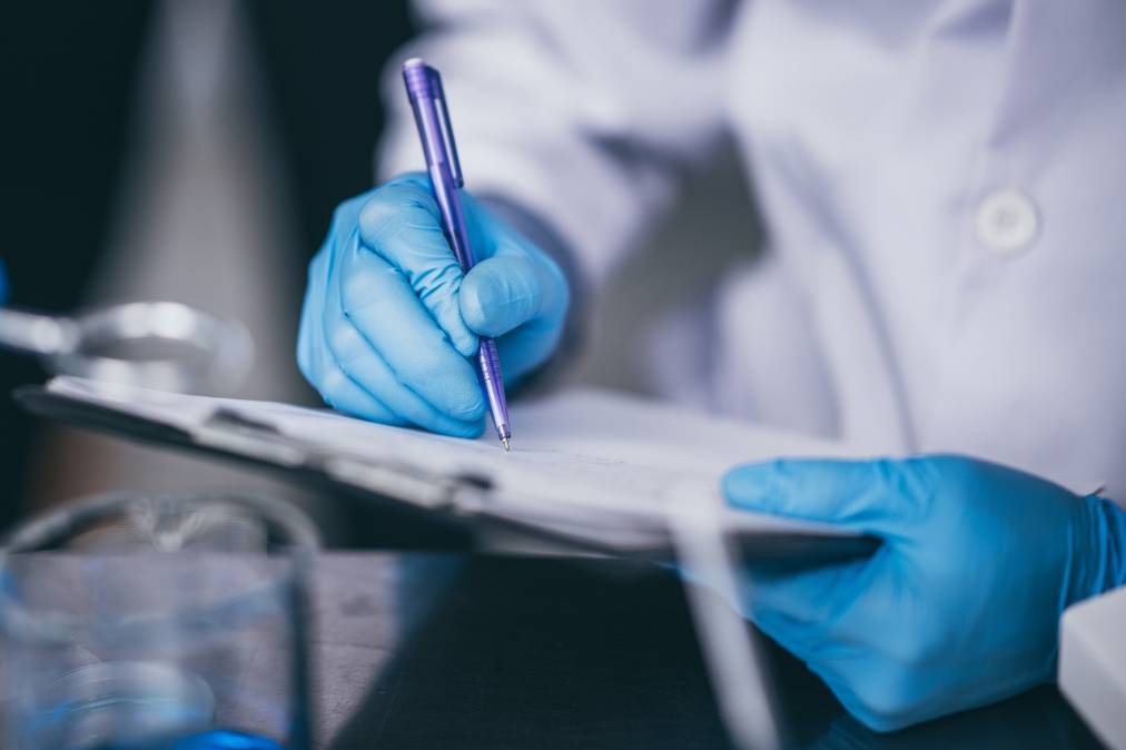 Hands in research lab coat holding a pen and pad.