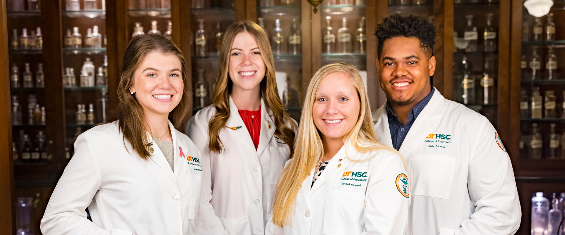 Four students standing in front of an apothecary cabinet.