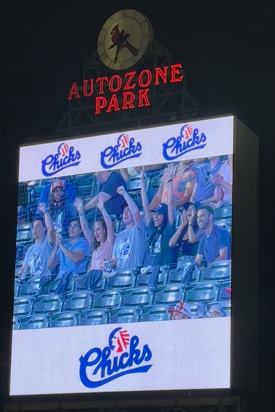 Residents wave and cheer as they appear on the video board during a Memphis Chickas baseball game at AutoZone Park at night