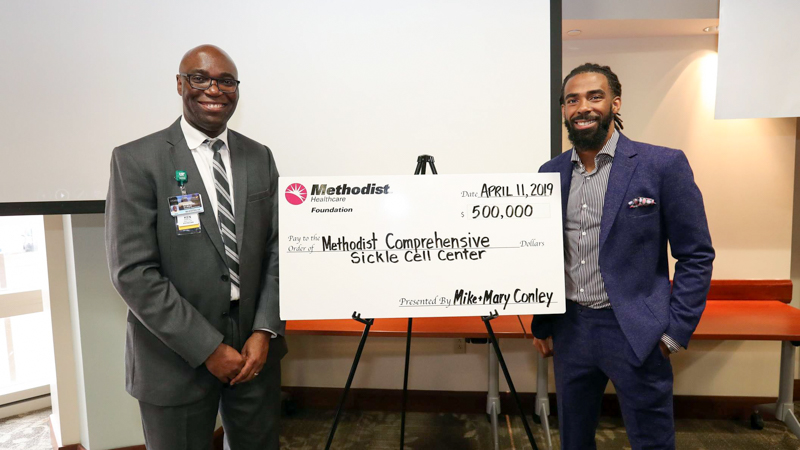 Dr. Ataga poses for a photo with Mike Conley at press event with donation check. 