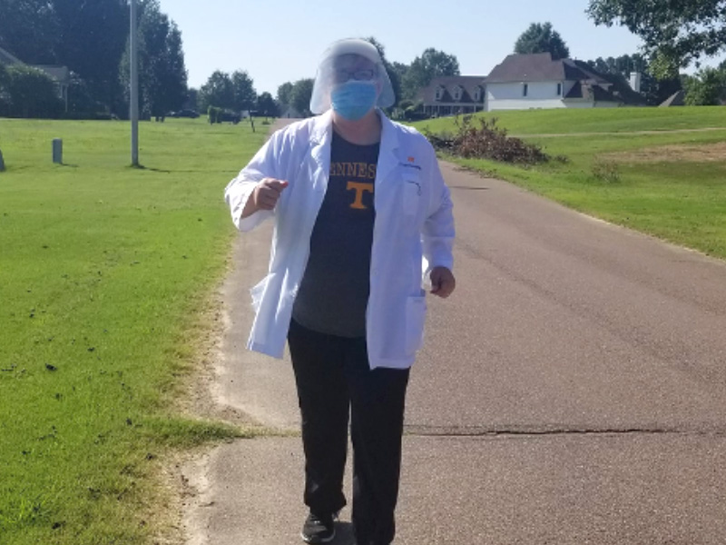 person in white coat walking outside with mask on